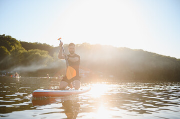 Sportsman kneeling on sup board paddling on lake at sunset