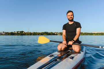 Sportsman kneeling on sup board paddling on lake in summer