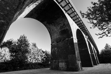 Low angle monochrome view showing the arches and texture of a large brick railway viaduct with...