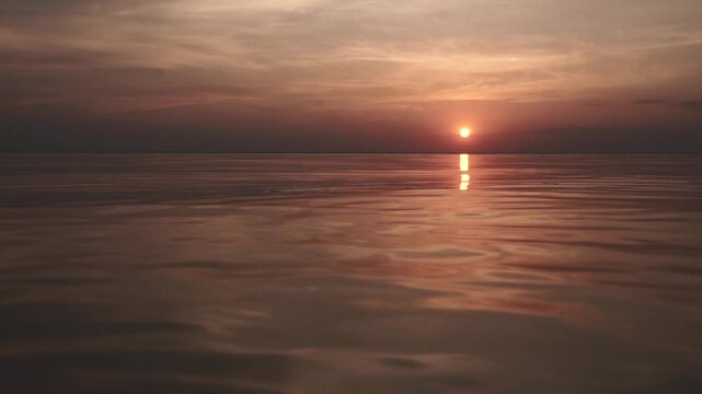 A peaceful sunset over the calm sea. Vibrant orange and blue gradient sky reflects on still water. Minimalist seascape filmed at twilight, ideal for background or meditative footage.
