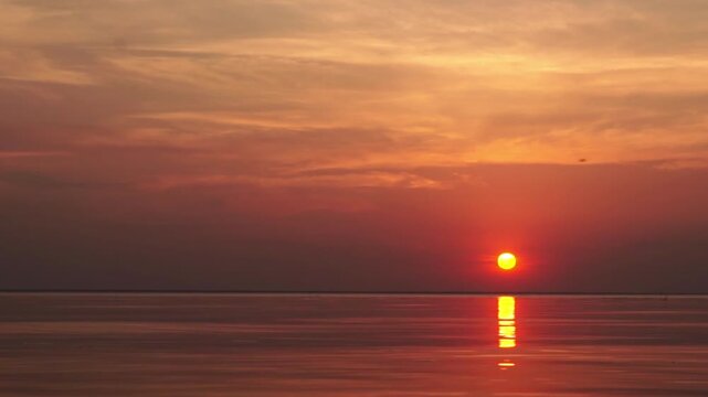 A peaceful sunset over the calm sea. Vibrant orange and blue gradient sky reflects on still water. Minimalist seascape filmed at twilight, ideal for background or meditative footage.