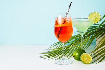 Margarita and Aperol Spritz at blue background with palm leaves. Summer cocktails.