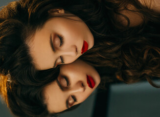 Model lies on mirror eyes closed. Close-up portrait princess. Bright evening make up red lips brown shine glitter shadows. Elegant wavy hairstyle long healthy hair brunette. face mirroring backdrop