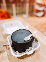 Unique black dessert served in a takeaway container on a wooden table