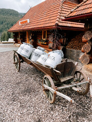Old wooden cart carrying large canisters outside a rustic mountain lodge in the forest