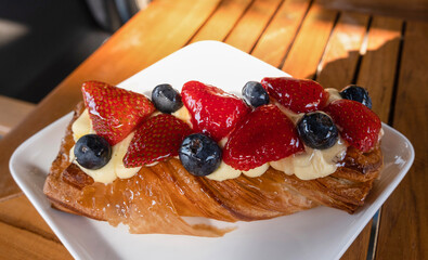 Croissant with cream, blueberries and strawberries lies on a plate, on a table, in a summer cafe