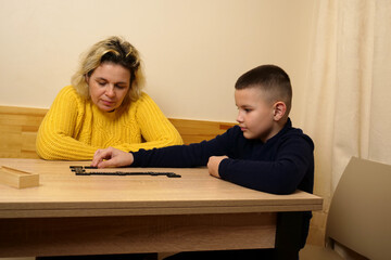 Mother and son playing dominoes at the table. Home recreation.