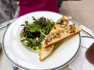 A plate of food with a salad and bread on it. The bread is cut in half and has a few pieces of pepper on it