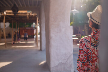 Fototapeta premium Young woman in an ethnic dress and hat exploring Al Seef Park in Dubai. Surrounded by traditional Emirati architecture and modern vibes, she enjoys the charm of Dubai Creek's cultural heritage.