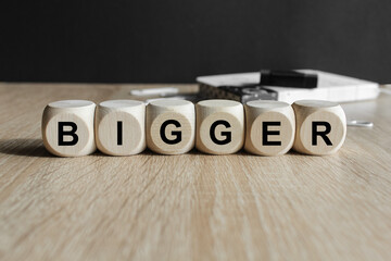 Wooden cubes with the word Bigger . Beautiful wooden table, black background. Growth development...