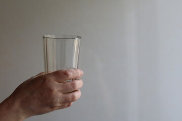 Hand holding a clear glass against a neutral background in a bright room