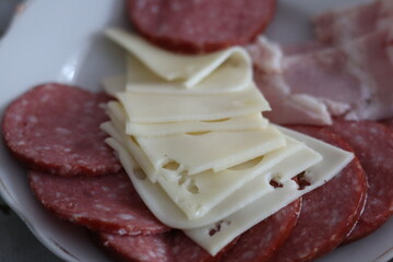 Cured meats and cheese displayed on a white plate in a cozy kitchen setting during afternoon...