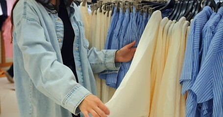 Woman selecting garment from rack in boutique, rack browsing repeated to showcase variety, mirror reflection framing fashion purchase thrill and shopaholic passion in modern retail environment