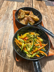 Two small pans featuring delicious roasted potatoes and vibrant sautéed mixed vegetables, presented as wholesome and flavorful side dishes.