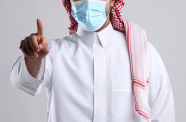 saudi arabian man in thob standing wearing face mask front facing showing index finger