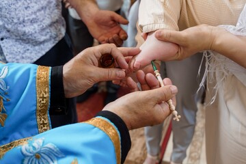 Eastern Orthodox Christian Baptism Ceremony: Priest Anointing Baby's Foot with Holy Oil in...