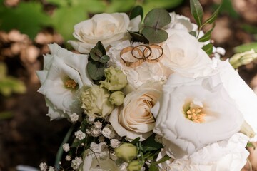 Elegant Wedding Rings on a White Rose Bouquet, Romantic Scene with Greenery and Natural Light,...