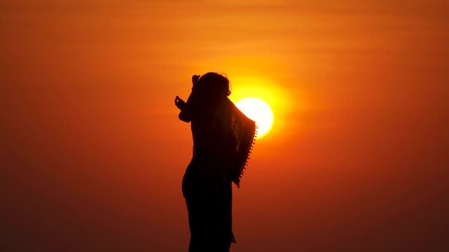 Silhouette shot of an Indian female tourist raising arms in front of sun during the sunset at Rann of Kutch in Kutch, Gujarat, India. Tourist enjoys sunset during winter in the desert of Kutch. 