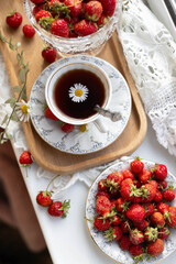 A charming arrangement features a cup of tea with a daisy floating on top, fresh strawberries scattered around. This cozy setup reflects a warm morning ambiance