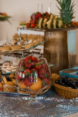 Elegant Dessert Table with Fresh Fruit Display, Pastries, Strawberries, Pineapple, Gold Accents, Silver Tablecloth, Party Buffet Setup.