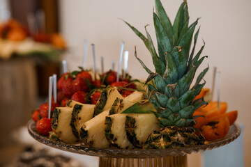 Vibrant Fruit Platter Display with Pineapple, Strawberries, Oranges, and Skewers on Elegant Glass...