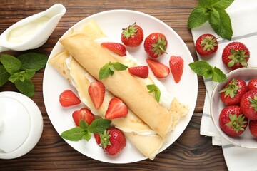 Tasty crepes with cream, strawberries and mint on wooden table, flat lay