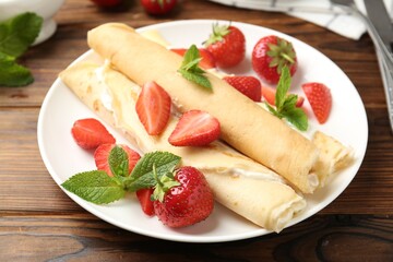 Tasty crepes with cream, strawberries and mint on wooden table, closeup