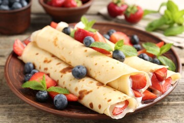 Tasty crepes with berries, cream and mint on wooden table, closeup