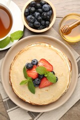 Delicious crepes with berries, cream, mint, honey and tea on wooden table, flat lay