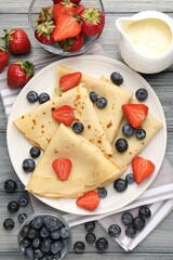 Delicious crepes with berries and cream on grey wooden table, flat lay