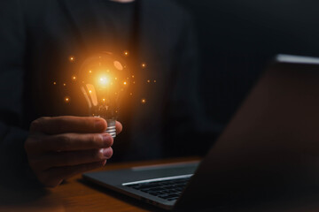Idea great innovate and concept. Businessman holding a light bulb shines in front of the laptop,...