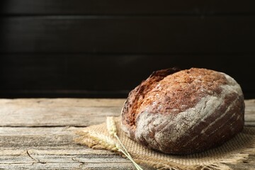 Loaf of fresh bread and spikes on wooden table, closeup. Space for text