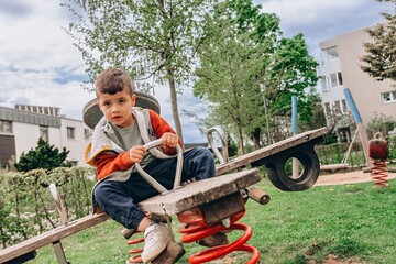 5 year old boy happily swings on a playground swing outdoors. A joyful moment of childhood fun,...