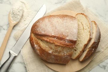 Pieces of fresh bread, flour and knife on white marble table, flat lay