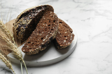 Pieces of fresh rye bread with seeds and spikes on white marble table, closeup. Space for text