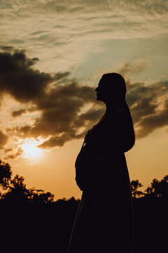 beautiful silhouette of pregnant woman with long hair at sunset , clouds and sky. third trimester of pregnancy, expecting baby, health of expectant mother and child. walk on summer day. shadows