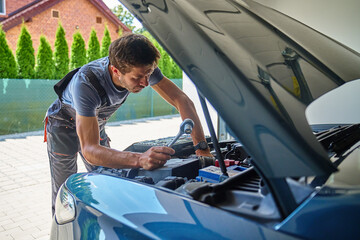 Male mechanic working on car engine with wrench under open hood in garage. Man in work overalls is...
