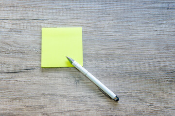 Blank yellow note on a wooden desk and a pen