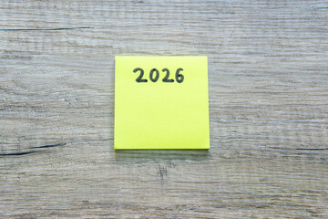 Yellow post-it with the number 2026 written on it. New Year 2026. on wooden desk. Concept: list of...