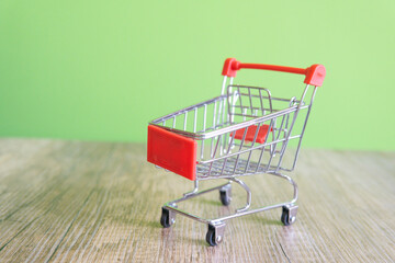 A shopping cart is on a wooden table. The cart is silver and red