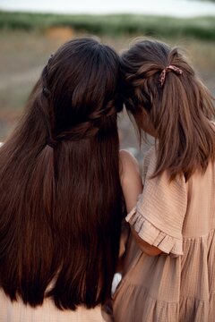 cute touching photo-beautiful long hair of mother and daughter, equally braided. girl cuddles up to mom, hugs. love in family, view from back. genetic factors of hair growth, care of children's hair