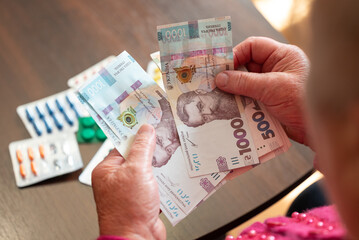 Senior woman counting hryvnias beside pills. Elderly woman counting Ukrainian hryvnias near nearly...