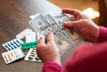 Senior woman counting dollars next to pills. Elderly woman holding US dollars after medicine...