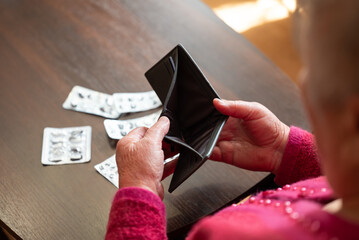 Elderly woman looking into empty wallet. Senior woman holding empty wallet with used pill packages on table, symbolizing poverty and unaffordable healthcare