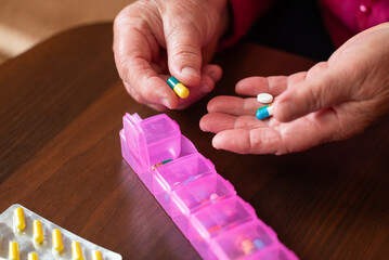 Elderly woman organizing pills in daily box. Senior woman preparing pills in weekly pill organizer for routine use