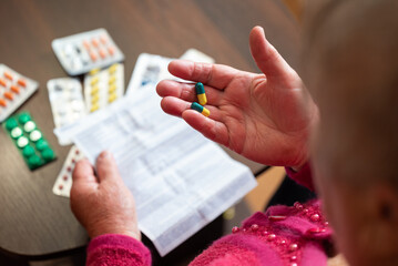 Senior woman reading instruction before taking pills. Elderly woman holding capsules and reading instruction before taking medicine