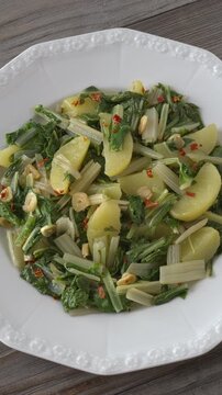 South Croatian Blitva s Krumpirom dish on a white plate. The dish is made with boiled potatoes, swiss chard, garlic, and olive oil. Table spin, vertical video.