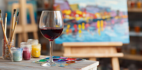 A glass of red wine and an easel with colorful paintings on it