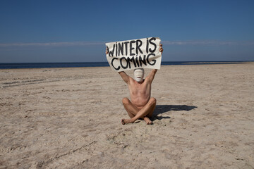 
Naked man in gas mask standing on a deserted beach, holding signs.