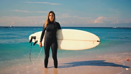 A woman in a wetsuit holding a surfboard, preparing to go into the water at the beach.